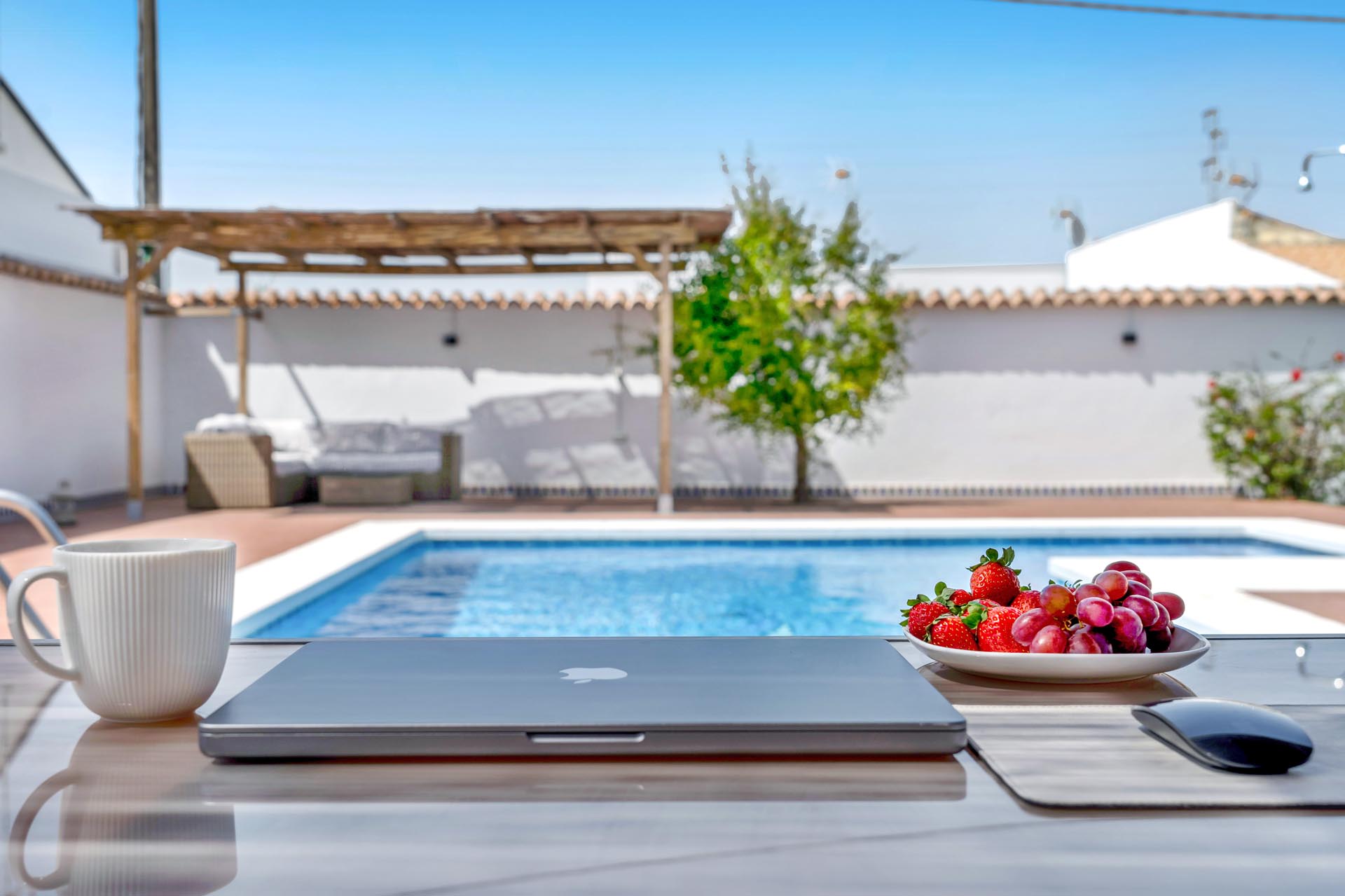 Portátil y taza de café, al fondo piscina y muebles de patio